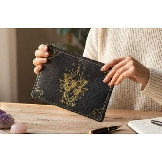The Witches' Quest black canvas zipper pouch featuring an intricate gold moth illustration held by a person.