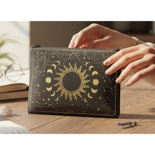 The Witches' Quest black canvas zipper pouch featuring a gold celestial sun and moon design on a wooden desk.