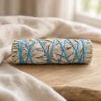 Ethically sourced California white sage smudge stick wrapped in blue string on a wooden surface