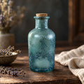 Six inch blue textured glass apothecary bottle with cork stopper on a wooden table