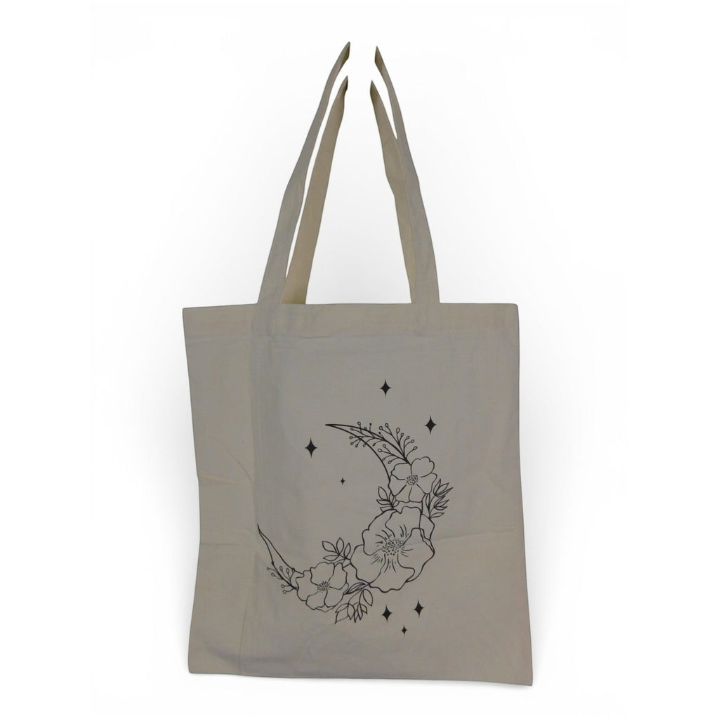 The Witches' Quest beige canvas tote bag featuring a black line art crescent moon, floral, and star graphic.
