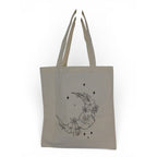 The Witches' Quest beige canvas tote bag featuring a black line art crescent moon, floral, and star graphic.