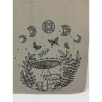 The Witches' Quest beige canvas tote bag featuring black line-art of mushrooms, butterflies, and celestial moon motifs.