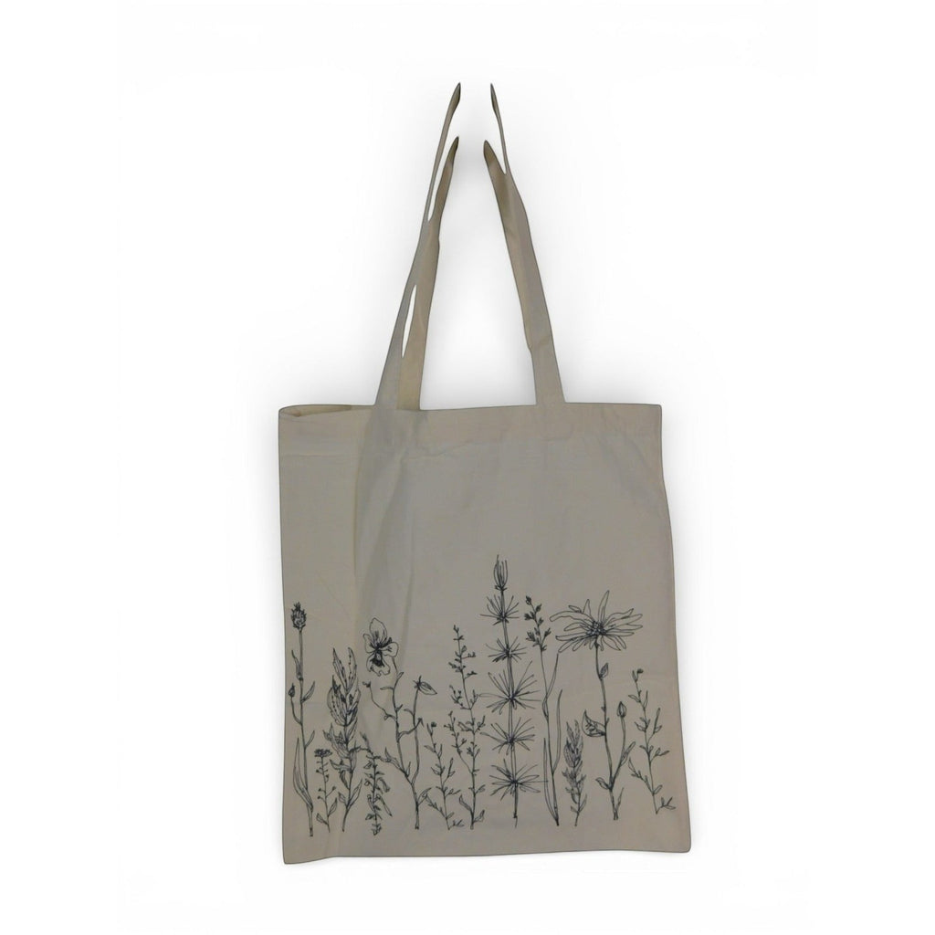 The Witches' Quest large beige cotton canvas tote bag featuring black wildflower line art illustrations on the front.