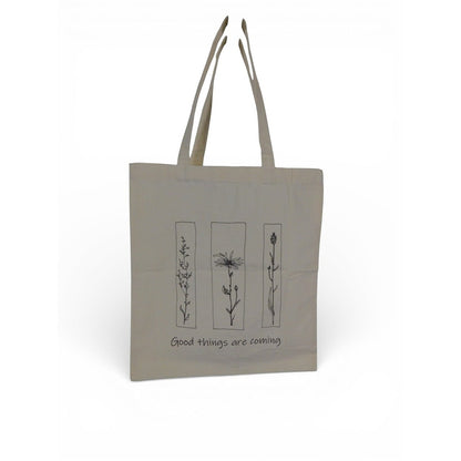 The Witches' Quest beige canvas tote bag featuring black floral line art and the quote Good things are coming