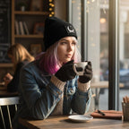 The Witches' Quest black ribbed knit beanie with crescent moon patch worn by a woman with pink-tipped hair in a cafe