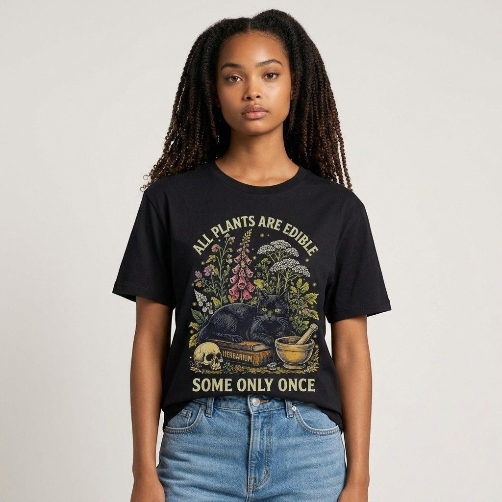 The Witches' Quest black cotton t-shirt featuring a botanical cat graphic with the text All Plants Are Edible