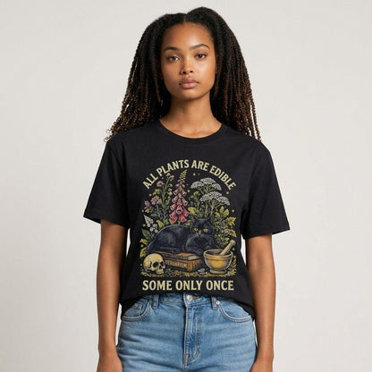 The Witches' Quest black cotton t-shirt featuring a botanical cat graphic with the text All Plants Are Edible