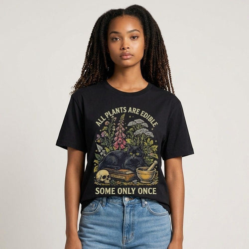 The Witches' Quest black cotton t-shirt featuring a botanical cat graphic with the text All Plants Are Edible