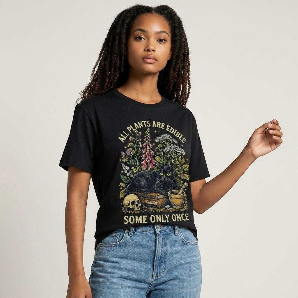 The Witches' Quest black cotton t-shirt featuring a cat, skull, and floral graphic with All Plants Are Edible text.