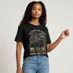 The Witches' Quest black cotton t-shirt featuring a cat, skull, and floral graphic with All Plants Are Edible text.