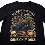 The Witches' Quest black cotton t-shirt featuring a graphic of a black cat, skull, and plants with text.