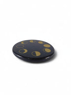 The Witches' Quest round black stone incense holder with gold celestial moon phase design and central stick hole.