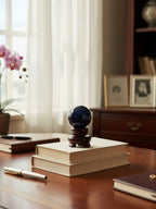 The Witches' Quest polished black obsidian sphere on a dark wooden stand resting on books in a sunlit room.