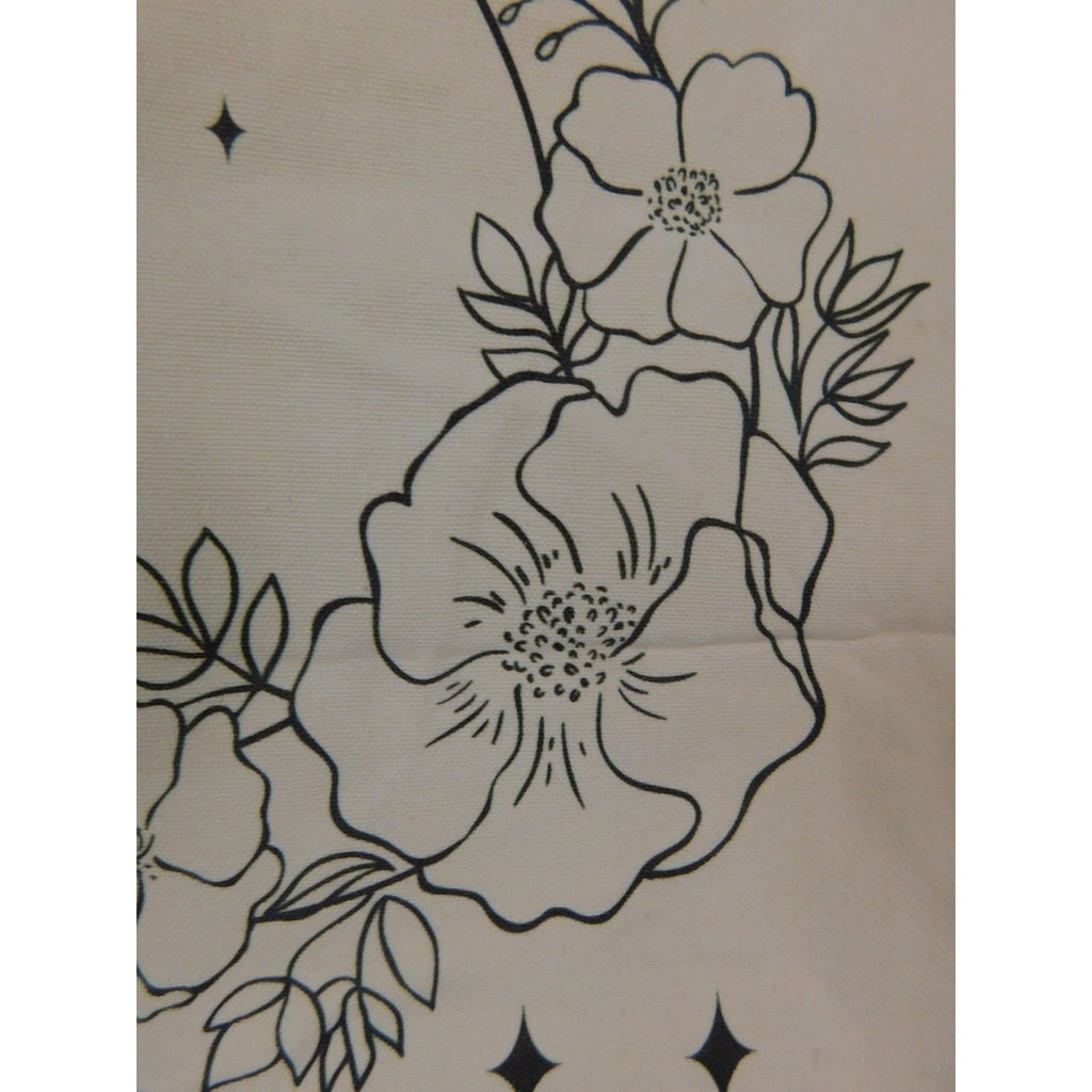 The Witches' Quest beige canvas tote bag featuring black line art of flowers, leaves, and stars in a crescent shape.