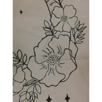 The Witches' Quest beige canvas tote bag featuring black line art of flowers, leaves, and stars in a crescent shape.