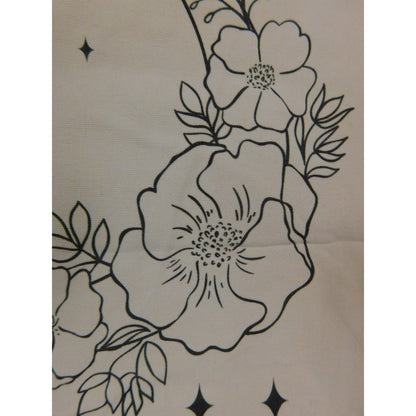 The Witches' Quest beige canvas tote bag featuring black line art of flowers, leaves, and stars in a crescent shape.