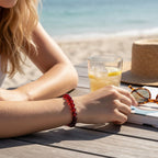 The Witches' Quest natural carnelian 8mm beaded stretch bracelet worn on a woman's wrist at a sunny beachside table.