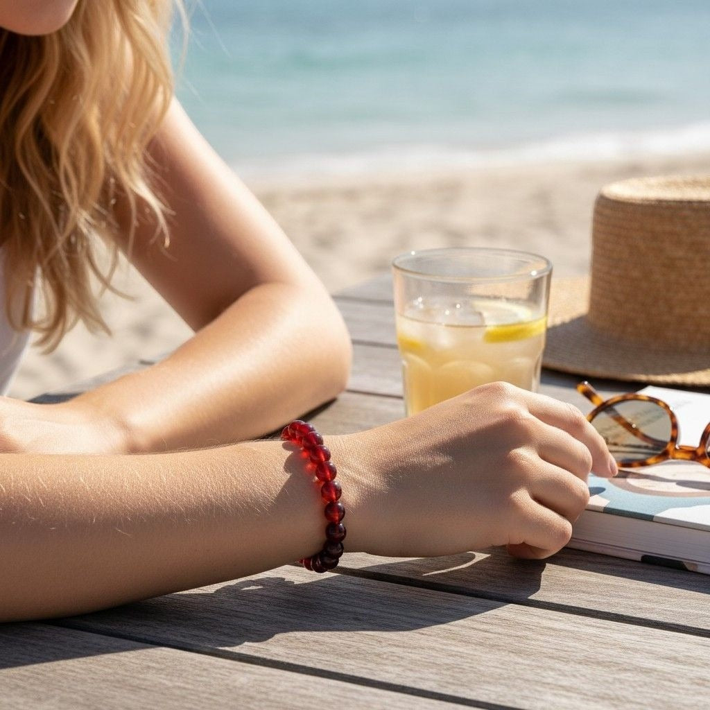 The Witches' Quest natural carnelian 8mm beaded stretch bracelet worn on a woman's wrist at a sunny beachside table.