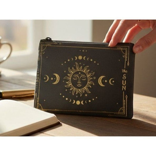 The Witches' Quest black canvas zippered pouch featuring a gold celestial sun and moon design on a wooden desk.