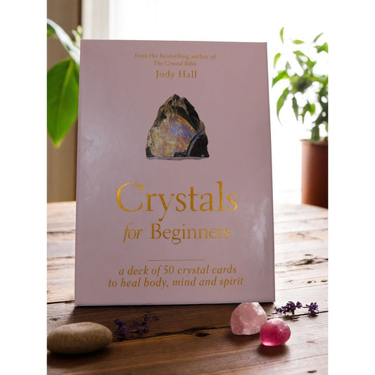The Witches' Quest Crystals for Beginners deck of 50 instructional cards in a soft pink box on a wooden table.