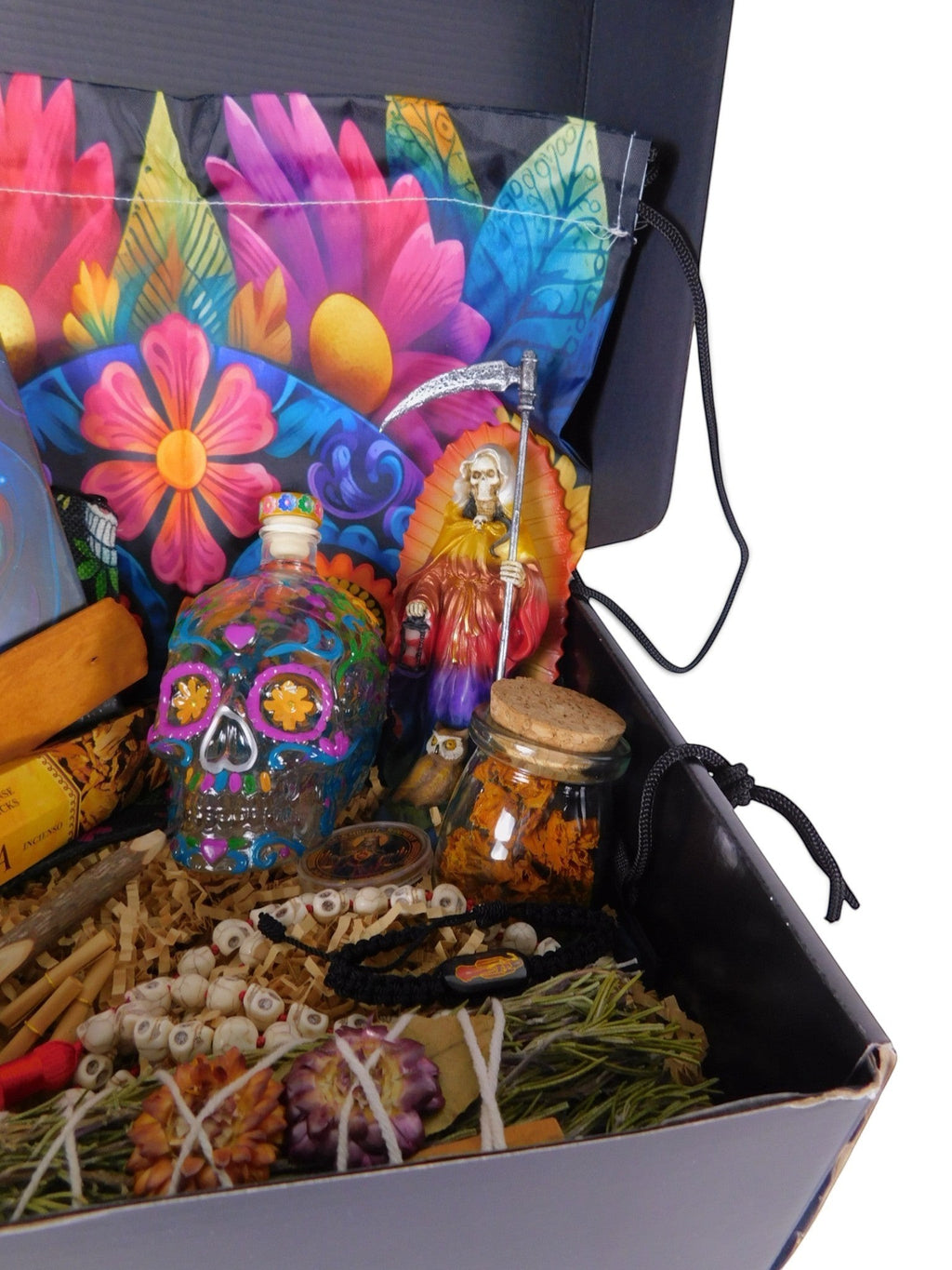 The Witches' Quest Day of the Dead altar box featuring a rainbow Santa Muerte statue, skull decanter, and marigolds.