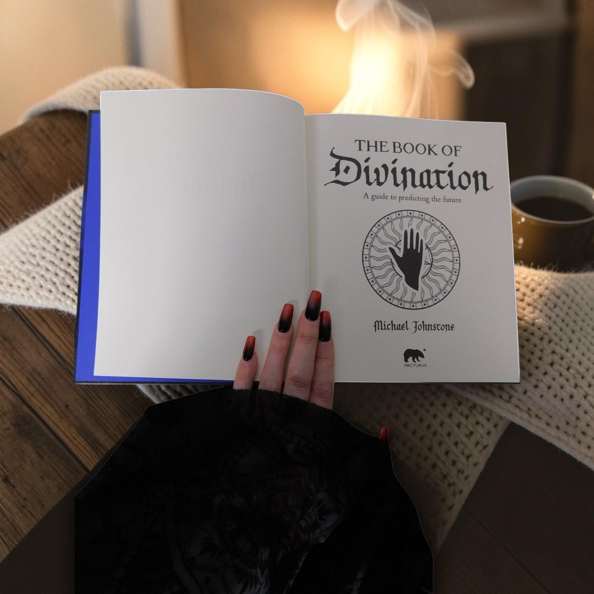 The Witches' Quest hardcover Book of Divination held open, showing the title page with palmistry illustration.