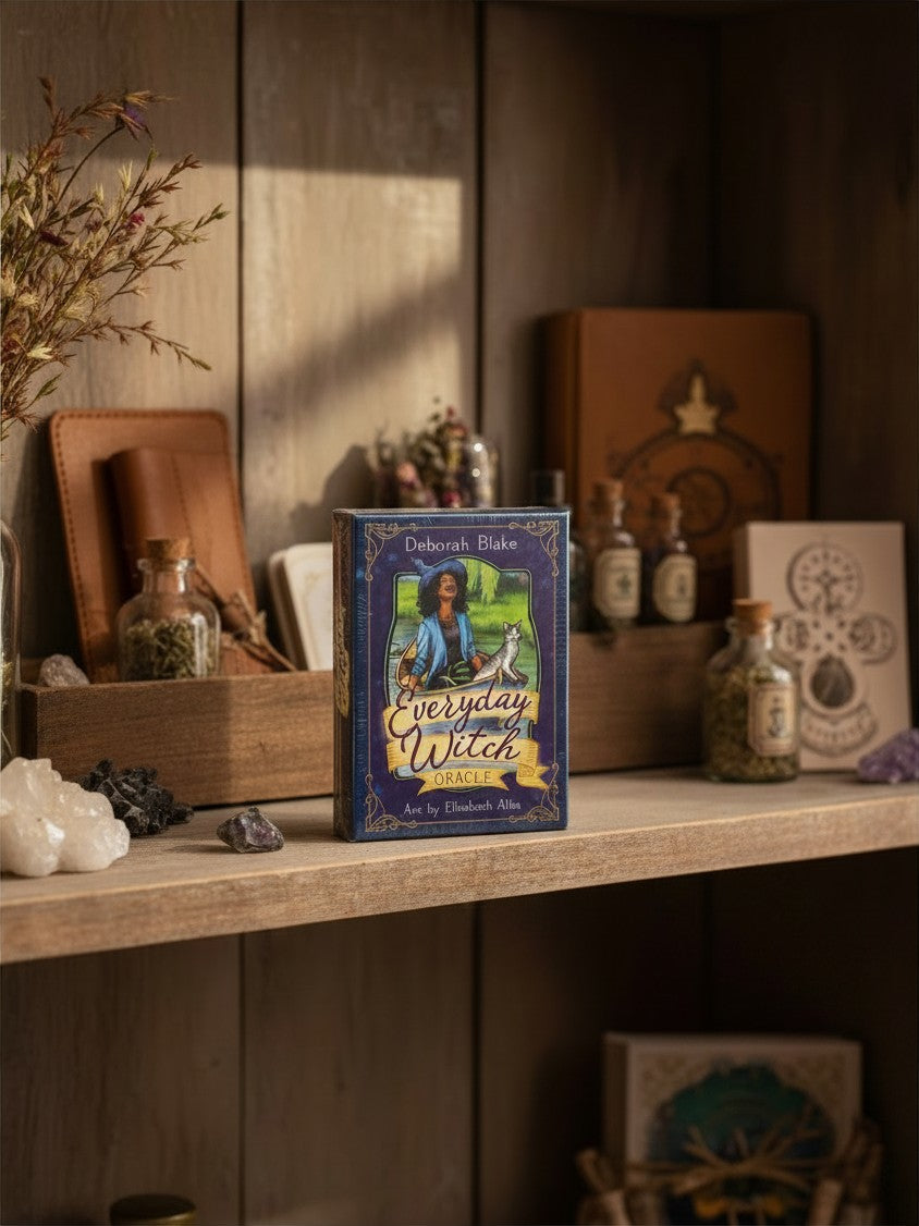 The Witches' Quest Everyday Witch Oracle deck box featuring whimsical witch and cat artwork on a rustic wooden shelf.