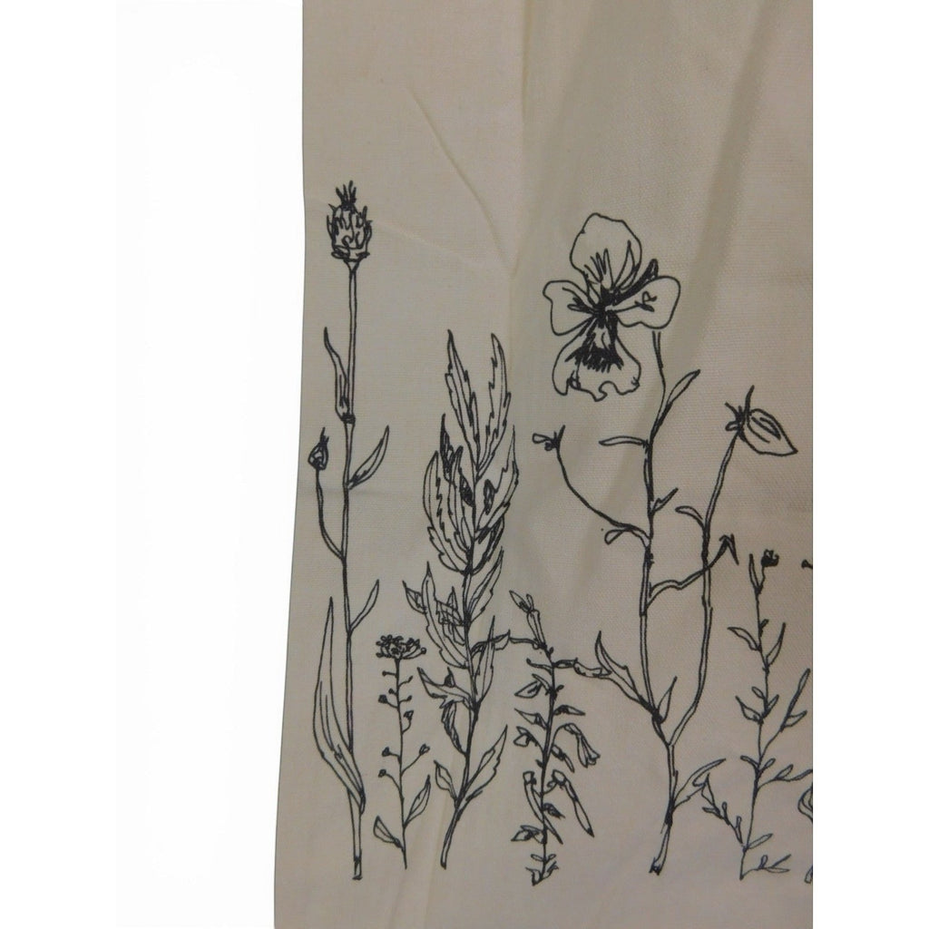 The Witches' Quest beige canvas tote bag featuring black botanical wildflower line art illustrations on the front.