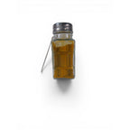 The Witches' Quest Ash & Sea Gold Dust ritual blend in a clear glass shaker bottle with a metal lid and hanging tag.