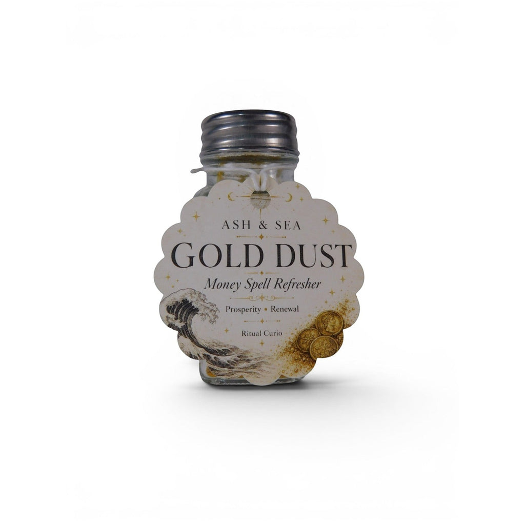 The Witches' Quest Ash & Sea Gold Dust money spell refresher in a clear glass shaker bottle with a decorative label.