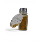 The Witches' Quest Ash & Sea Gold Dust ritual blend in a clear glass shaker bottle with a decorative prosperity label.