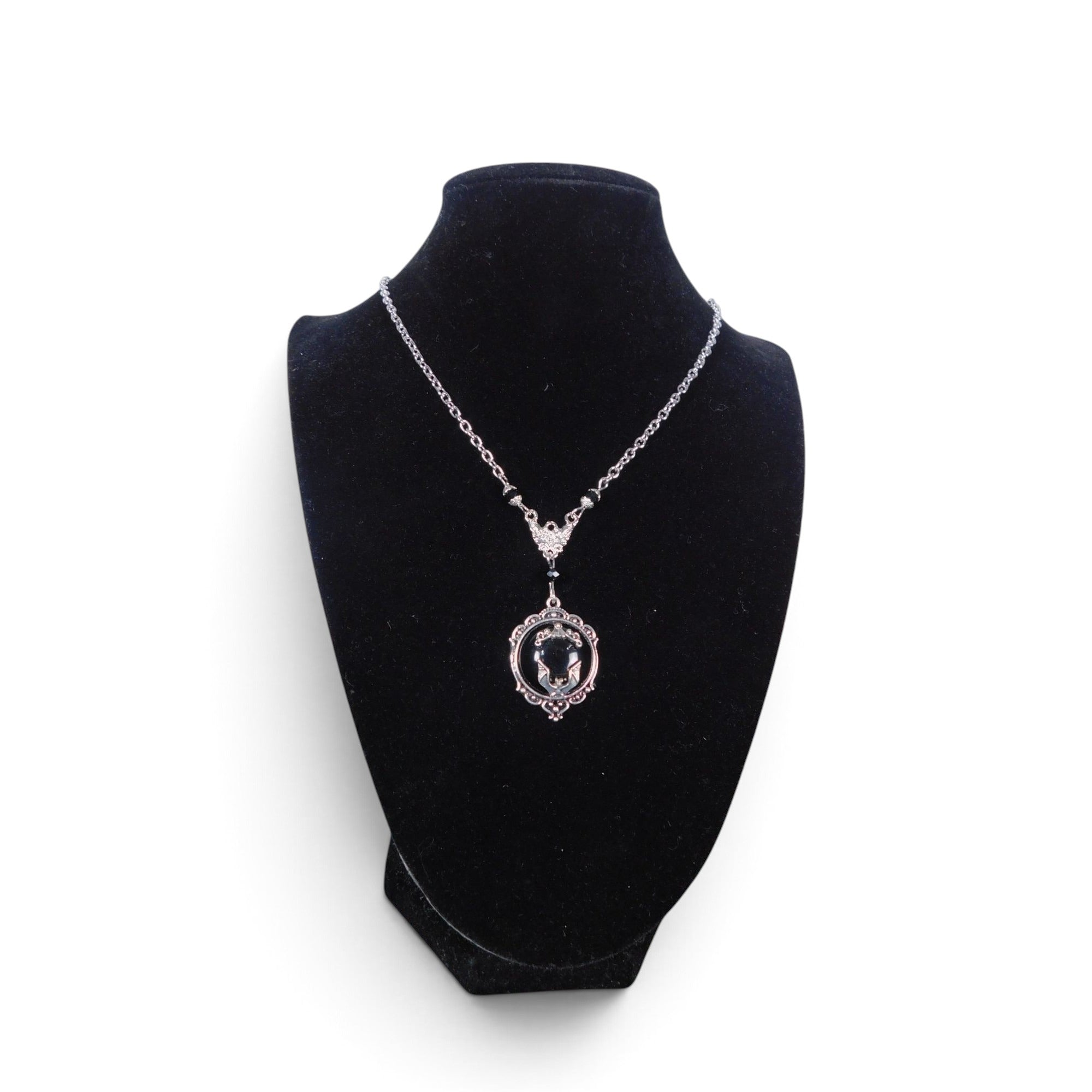 The Witches' Quest Victorian gothic bat cameo necklace in silver-tone alloy with a black resin backdrop on a display.