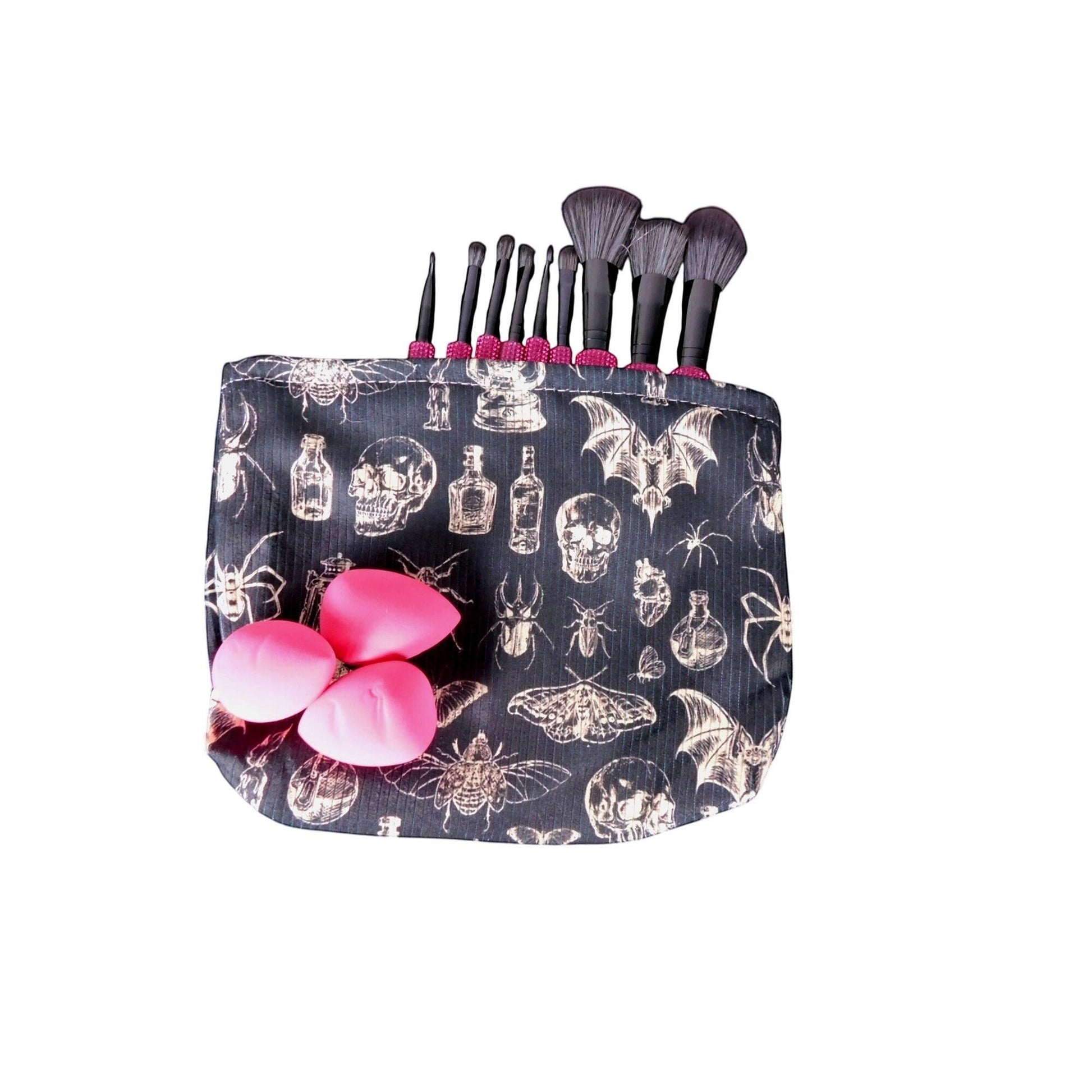 The Witches' Quest gothic makeup bag in black fabric with skull and insect print, holding brushes and pink sponges.