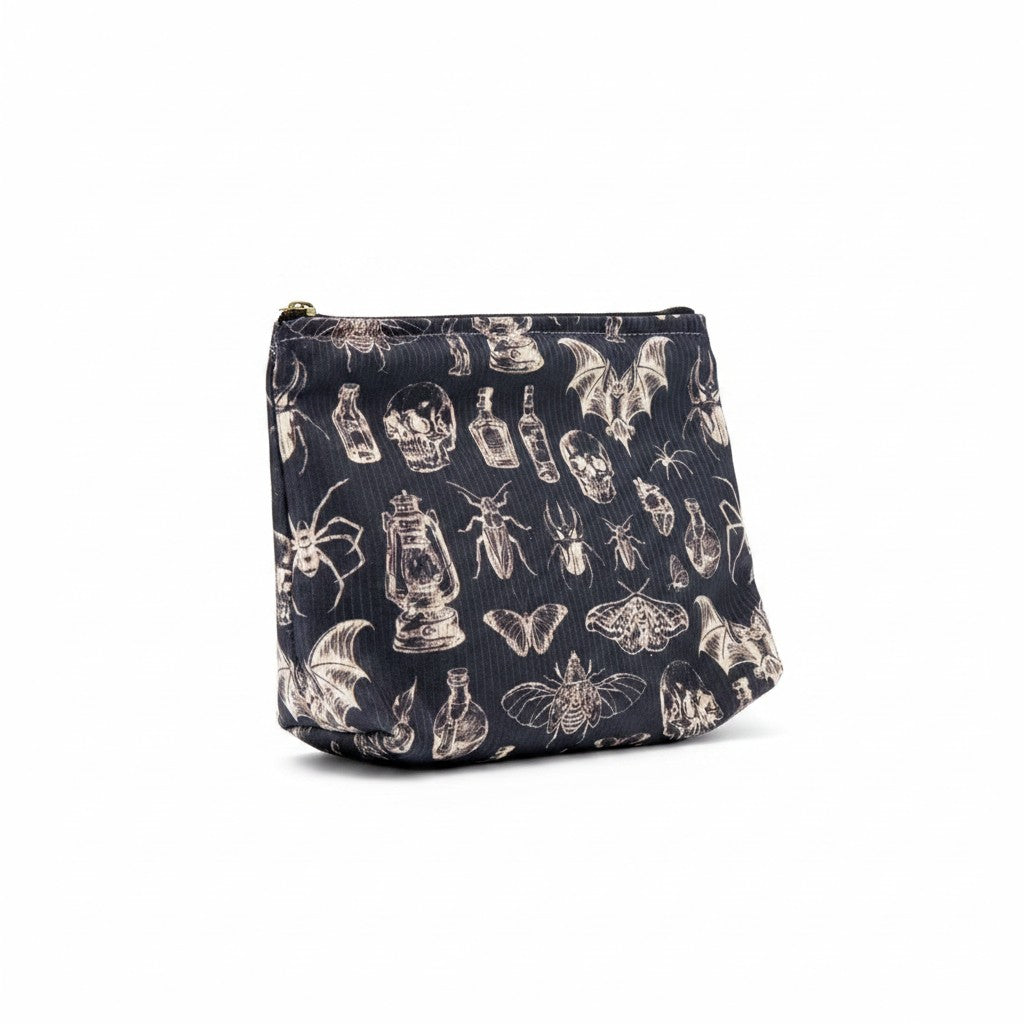 The Witches' Quest gothic makeup bag in black fabric with a white skull, insect, and lantern print and zipper closure.