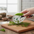 The Witches' Quest green herb mezzaluna knife with stainless steel blade and stem-stripping holes chopping fresh herbs.