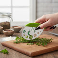 The Witches' Quest green herb mezzaluna knife with stainless steel blade and herb stem-stripping holes on wood board