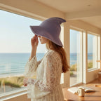 The Witches' Quest lavender purple knit witch hat with a wide brim worn by a woman in a white lace dress by the sea.