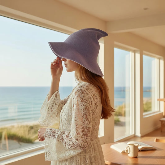 The Witches' Quest lavender purple knit witch hat with a wide brim worn by a woman in a white lace dress by the sea.