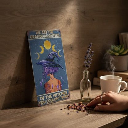 The Witches' Quest metal sign featuring a witch illustration, moon phases, and empowering text on a wooden desk.
