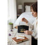 The Witches' Quest black canvas zipper pouch featuring a gold moon phase and hand design held by a woman at a desk.