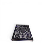 The Witches' Quest hardcover copy of The Book of Practical Witchcraft with a dark purple cosmic cover design.