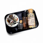 The Witches' Quest protection travel altar kit featuring a ritual candle, herbs, black salt, and onyx in a black tin.