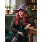 The Witches' Quest purple knit witch hat with a wide brim worn by a woman with long red hair in a cozy library setting