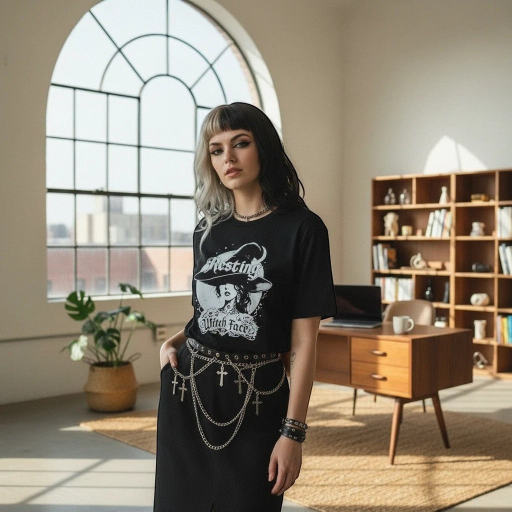 The Witches' Quest black cotton crew neck t-shirt with Resting Witch Face graphic worn by a woman in a bright studio.