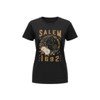 The Witches' Quest black cotton unisex t-shirt featuring a Salem 1692 graphic with a cat, moon, and floral design.