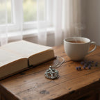 The Witches' Quest silver tone St. Brigid’s Cross pendant necklace on a wooden table with a book and steaming tea.