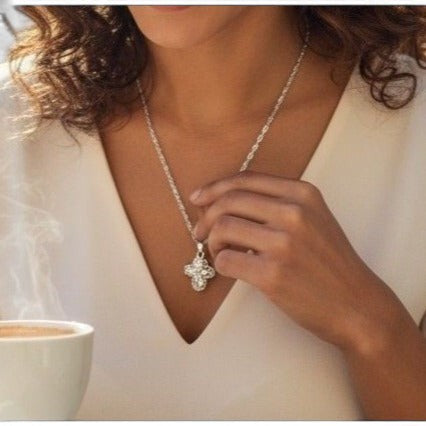 The Witches' Quest silver floral cross locket necklace with intricate filigree worn on a model holding a coffee cup.