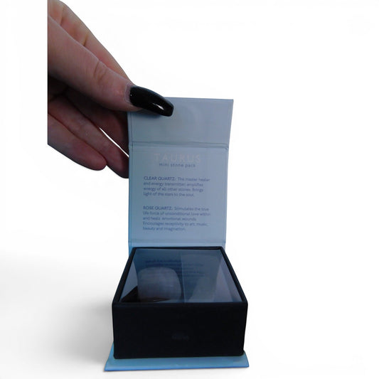 The Witches' Quest Taurus zodiac crystal stone pack featuring clear and rose quartz in a gift box held by a hand.