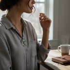 The Witches' Quest silver-tone Tree of Life pendant necklace worn by a woman in a grey shirt near a coffee mug.